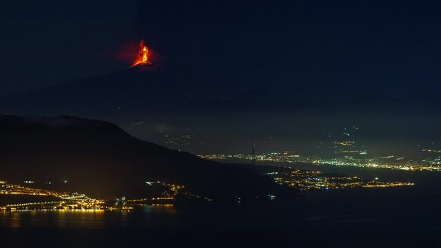 Timelapse of eruption of Mount Etna volcano at night time with sea and city lights in foreground seen from mainland on February 10 2022 , Sicily, Italy