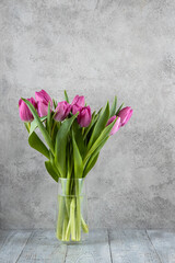 Colored Tulips in a vase on a grey wooden table.