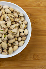 White bowl filled with pistachios.  Bamboo background.  Copy space on right.