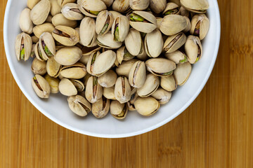 White bowl filled with pistachios.  Bamboo background.