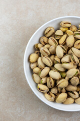 Top down view of a white bowl of pistachios on a tile surface.