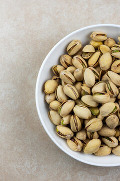 Top Down View Of A White Bowl Of Pistachios On A Tile Surface.