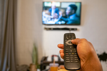 Close-up of man pushing the buttons on remote control to switch the channel on TV in the room