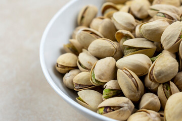 Fototapeta premium Side view of a white bowl of pistachios on a tile surface.