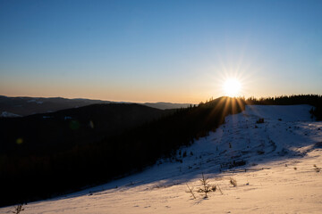 Fantastic sunrise in winter forest. Idyllic winter time. The bright sun rises over the pine forest.