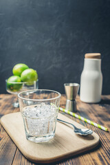 Ice for a cocktail and limes in glass on a wooden table.