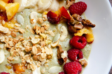Smoothie fruit bowl with banana, peaches, raspberries, nuts, granola and pumpkin seeds for breakfast. Tasty oatmeal with fruits in white plate. Delicious healthy breakfast.