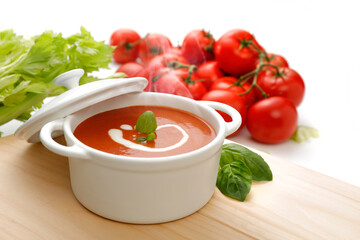 Italienische Tomatensuppe mit Sahne und Basilikum dekoriert, in weißer Keramik-Schale mit Zutaten im Hintergrund