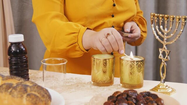 hand Jewish woman lights Shabbat candles on the table. Medium plan
