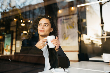 Young woman drinking coffee in a coffeeshop, through window