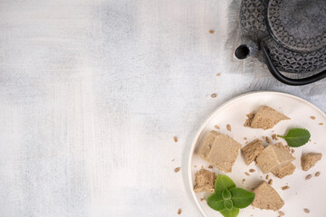 Traditional eastern sweets halva with sunflower seeds and mint leaves on a white plate. Brewing...