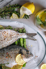 the concept of a delicious dinner for two from dorado. raw baked dorado fish with asparagus and lemon in spices