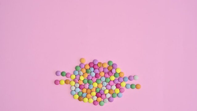 Rainbow colorful candies make Easter bunny shape on pastel pink background. Stop motion flat lay concept