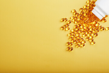 Gold Vitamin D3 capsules poured out of a jar on a yellow background with free space