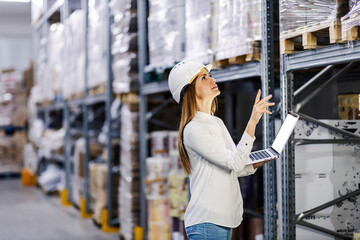 A supervisor looking at goods in warehouse and entering data in laptop.