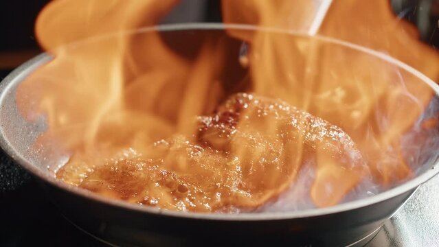 Chef frying ribs with flambe technique. Professional cheif cooking pork meat in restaurant kitchen. Delicious barbecue pork, mexican spicy cuisine, indian or arabian food.