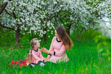 mother and daughter sit in the apple orchard in spring