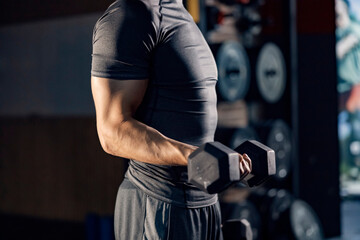 Unknown muscular man doing exercises for biceps with dumbbell in a gym.