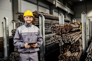 Portrait of a steel factory engineer working with tablet and smiling at the camera.