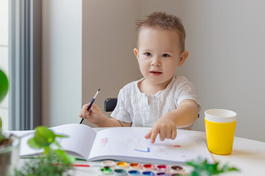 happy kid paints with a brush with watercolor paints, creativity and learning