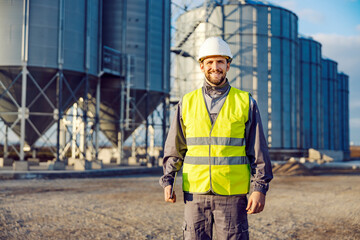 Portrait of a factory worker standing in front of silos full of grain or corn.