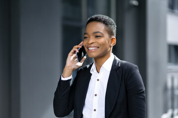 Cheerful african american business woman talking on her mobile phone near office building