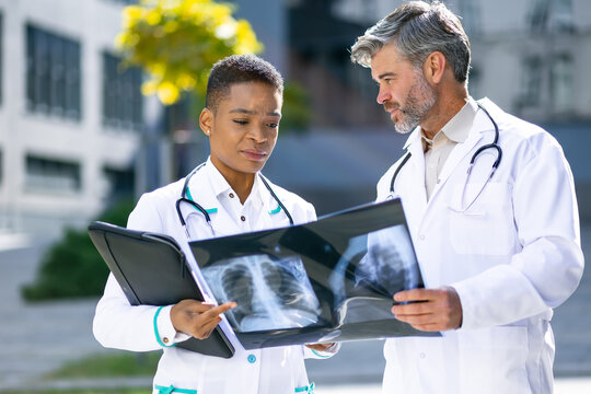focused doctors check x-ray, standing near hospital, discussing patient treatment