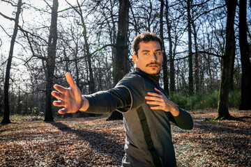Runner is doing stretching in the woods. Young man with blue eyes and mustache is training in the park.