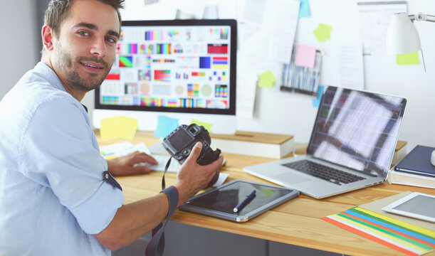 Portrait of young designer sitting at graphic studio in front of laptop and computer while working online.