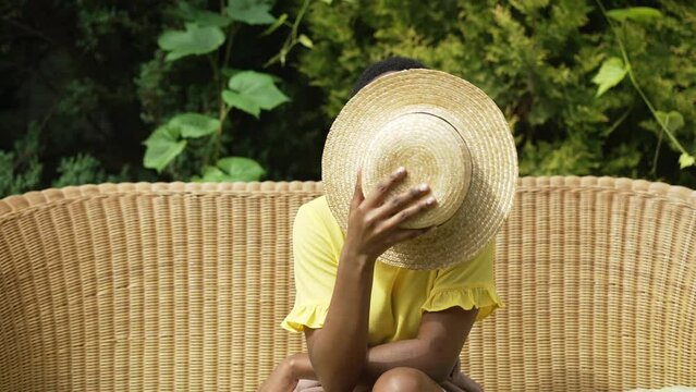 Front view confident young woman putting down straw hat smiling looking at camera. African American slim charming lady posing in slow motion flirting outdoors on sunny summer spring day