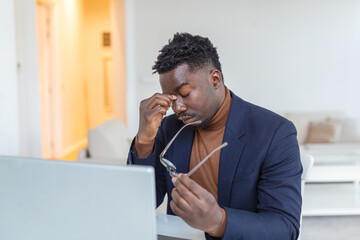 Tired African American businessman taking off glasses, exhausted employee massaging nose bridge, suffering from eye strain after long computer work, feeling pain, health problem concept