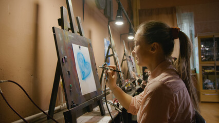 Woman artist learns to paint with airbrush with acrylic dye, paper and easel. Indoors. Concept...