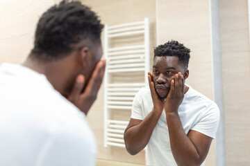 Morning hygiene, Handsome man in the bathroom looking in mirror. Reflection of Africanman with beard looking at mirror and touching face in bathroom grooming