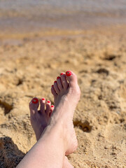 Female feet with red pedicure on yellow sand on the beach, close up