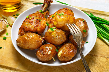 tasty lunch in rural style, healthy food - glass of beer, fried chicken meat and unpeeled roasted potatoes on a dish, green leek, salt and garlic, cooked food on a white wooden boards