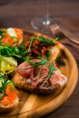 Bruschetta with prosciutto, cheese, tomatoes, herbs on a wooden board. Tasty breakfast.