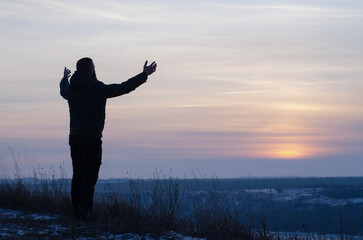 Pray. Repentance. Silhouetted men on a background of blue sky and sunset. Kneeling Prayer to God. Glorification. Praising God. A man with his hands up. Worship God
