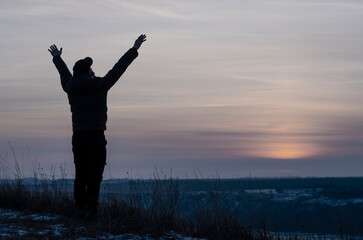 Fototapeta na wymiar Pray. Repentance. Silhouetted men on a background of blue sky and sunset. Kneeling Prayer to God. Glorification. Praising God. A man with his hands up. Worship God 
