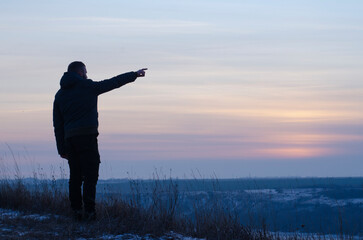 Fototapeta premium Silhouette of a man against the backdrop of sunset, sky. Man pointing his finger