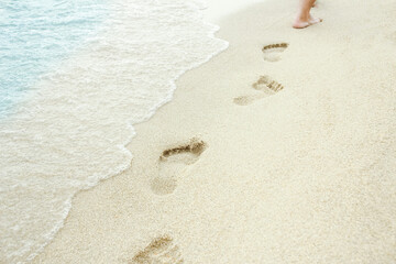 A Beach travel - woman relaxing walking on a sandy beach leaving footprints in the sand. Close up detail of female feet on golden sand at a beach in Greece. Background.