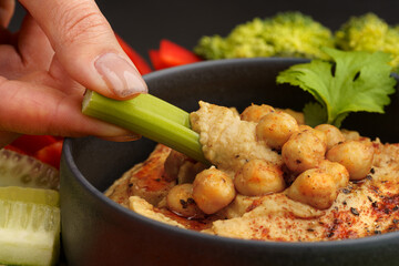 Closeup of hand with celery stick with chickpeas hummus. Tasty hummus with vegetables and smoked...