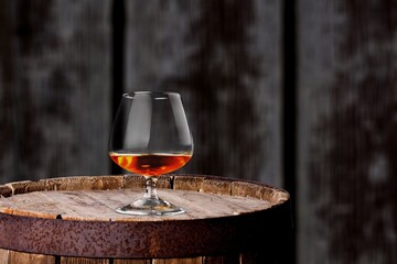 Glasses of alcohol stand on barrels of cognac in wine cellar illuminated by soft light