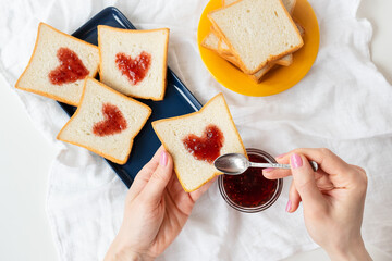 The girl makes a toast on which the heart is made of jam. Surprise breakfast concept in bed....