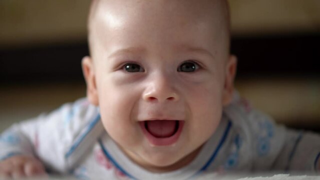Newborn Active Baby Cute Smiling Teethless Face Portrait Early Days On Stomach Developing Neck Control. 5 Months Child On White Bed Looking on Camera. Infant, Childbirth, Parenthood, Beginning Concept