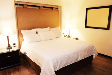 Habitación de hotel, cama, muebles, almohadas, sabanas blancas, sillas y sofá. Vista lateral