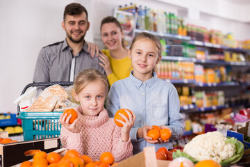 Fototapeta premium Cheerful little girl choosing fresh mandarins while shopping with parents in food store