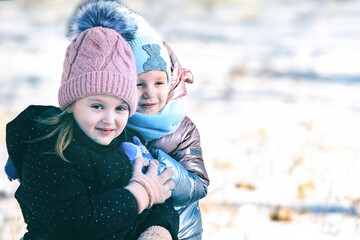 Obraz premium Portrait of two beautiful happy little girls on a walk in a winter park in warm clothes, hats and scarves