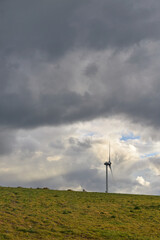 Fototapeta na wymiar wind energy tubin on top of a hill with large cloudy sky copy space