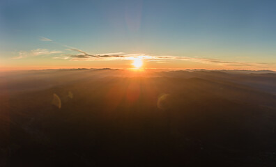 Aerial view of dark mountain hills with bright sunrays of setting sun at sunset. Hazy peaks and misty valleys in evening