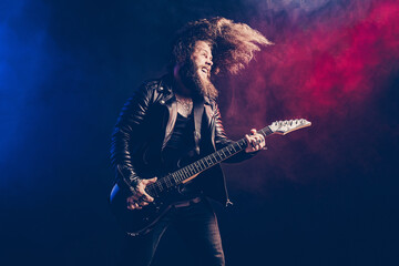 Expressive man rock guitar player with long hair and beard plays on the smoke background. Studio shot